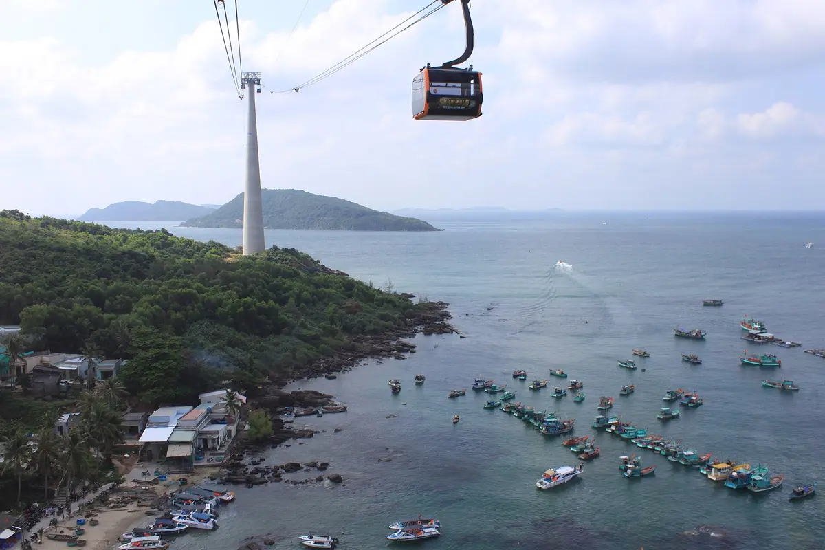 A cable car cabin and a pylon above a green headland, with fishing boats on the sea below