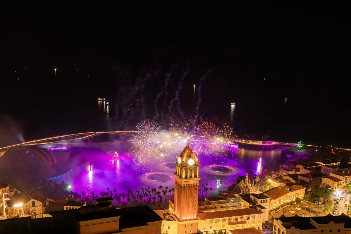 Fireworks and purple light over the bay at Sunset Town at night, with a lit red clock tower in the foreground